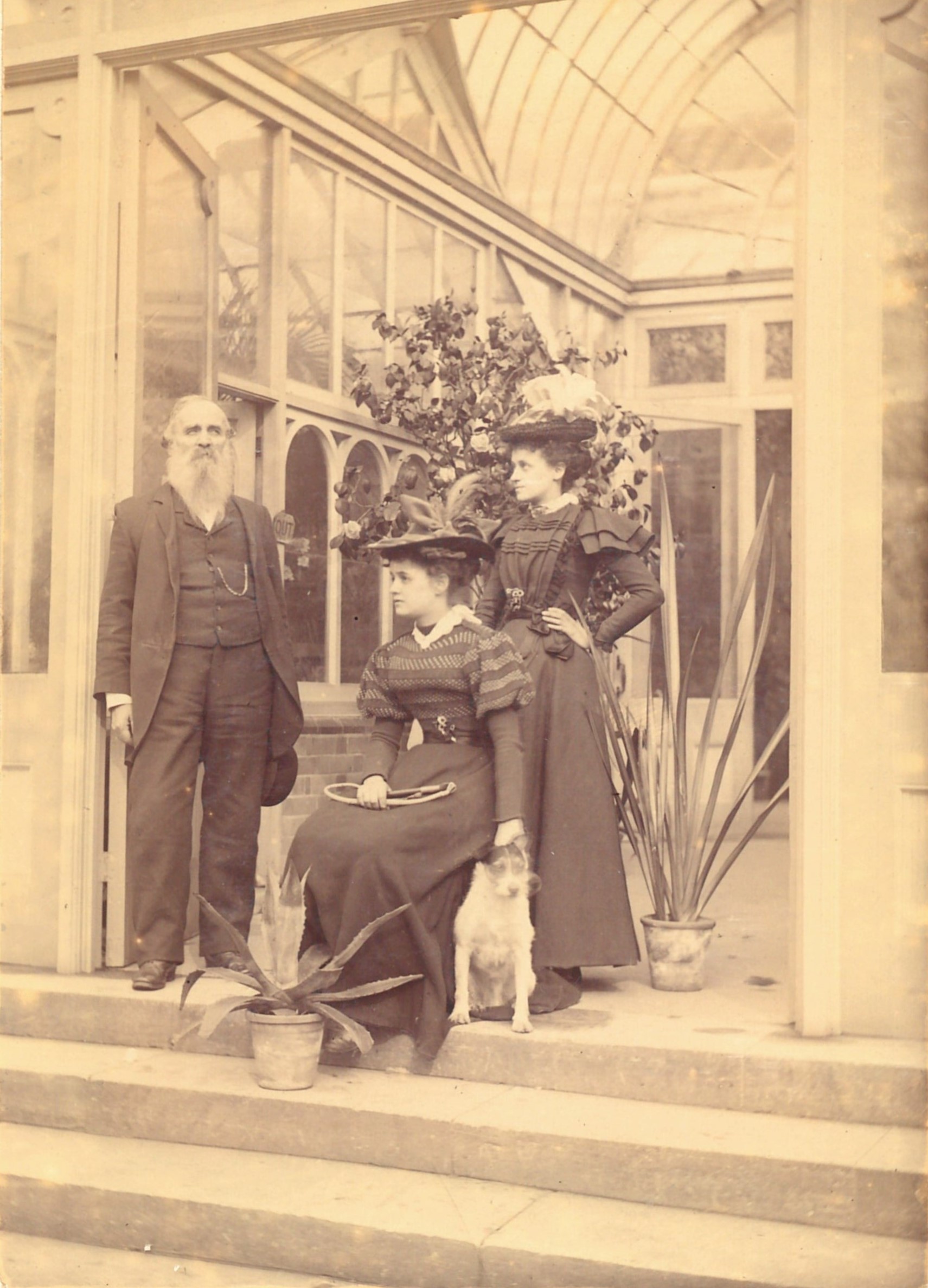 A sepia tone picture of William Latham, who is a man in a suit and his neices, Kate and Lizy who are in fancy dresses, and a dog.